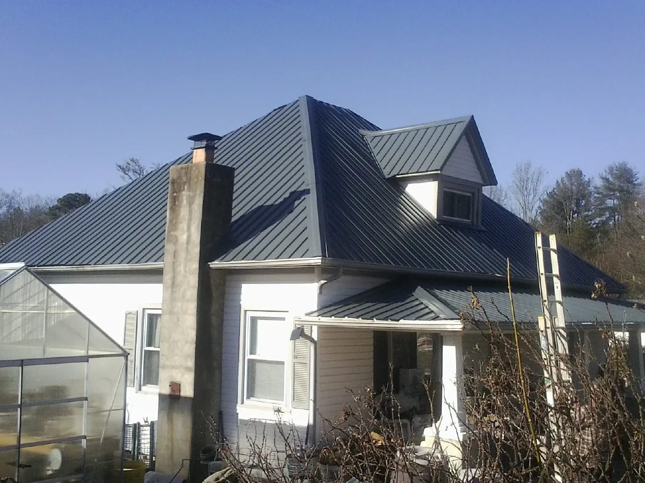 Dark blue standing seam metal roof on a white farmhouse with dormer — Slate & Tile Roof Repair by Roofing Brothers in Reynolds