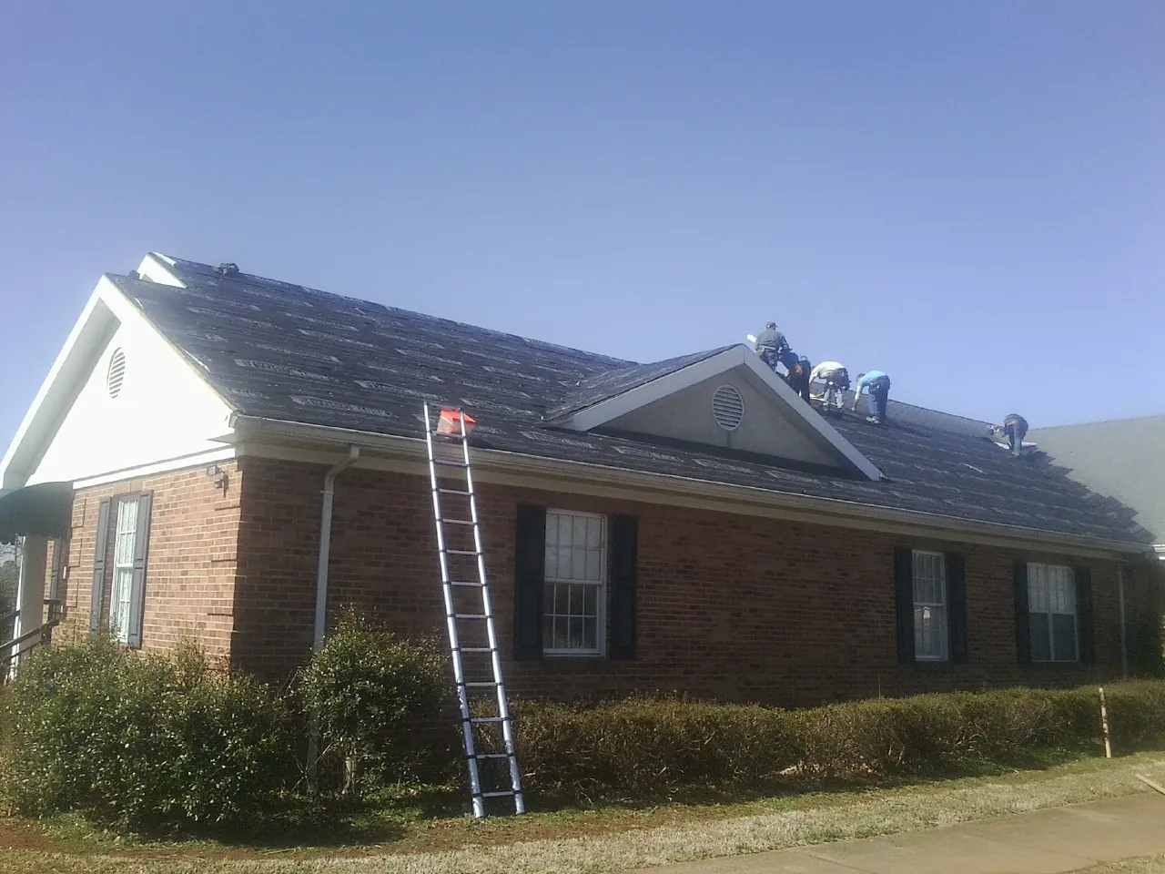 Crew tearing shingles off a brick ranch roof with a ladder set — Emergency Roof Repair work by our crew in Reynolds