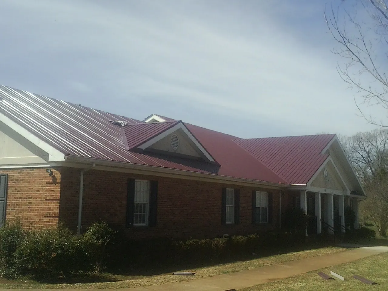 Red metal roof with gabled entries on a long brick building, from a Hail Damage Roof Repair job in Reynolds