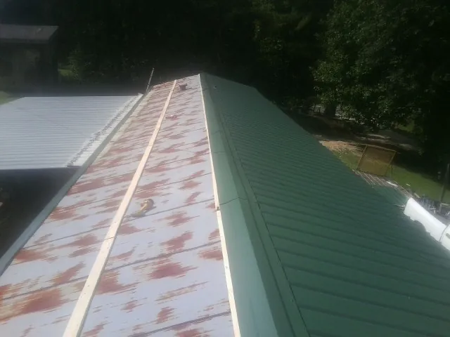 Old rusted panels beside newly installed green metal roofing — Wind Damage Roof Repair by Roofing Brothers in Reynolds