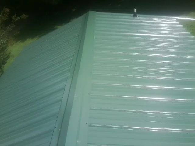 New green metal panels meeting at the ridge of a roof — Flat Roof Repair work by our crew in Reynolds